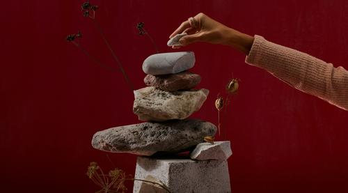 A vertical stack of stones with a hand placing a smaller rock on top.